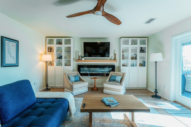 living room with visible vents, a glass covered fireplace, wood finished floors, baseboards, and ceiling fan