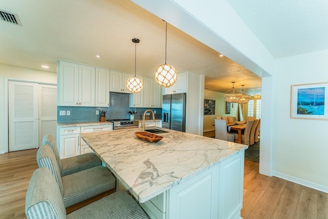 kitchen featuring visible vents, a sink, appliances with stainless steel finishes, white cabinets, and light wood finished floors