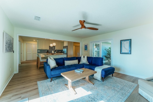 living area featuring visible vents, ceiling fan, baseboards, and light wood-style floors