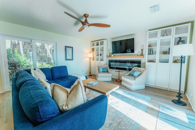 living room with visible vents, wood finished floors, a textured ceiling, and a glass covered fireplace