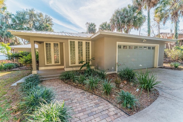 view of front facade with stucco siding, driveway, metal roof, and a garage