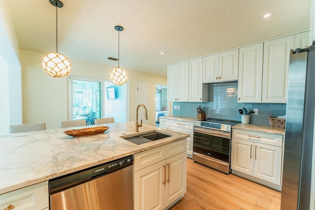 kitchen with light stone countertops, light wood-style flooring, a sink, decorative backsplash, and appliances with stainless steel finishes