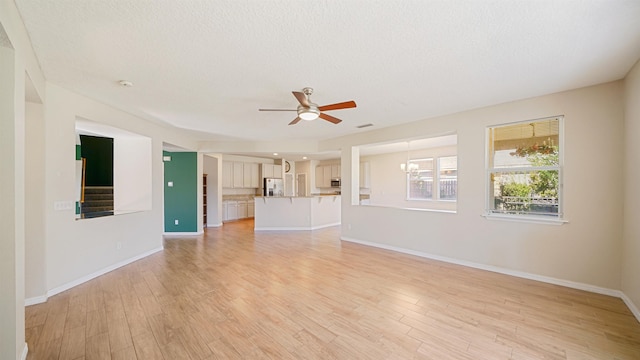 unfurnished living room featuring ceiling fan with notable chandelier, a textured ceiling, and light wood-type flooring