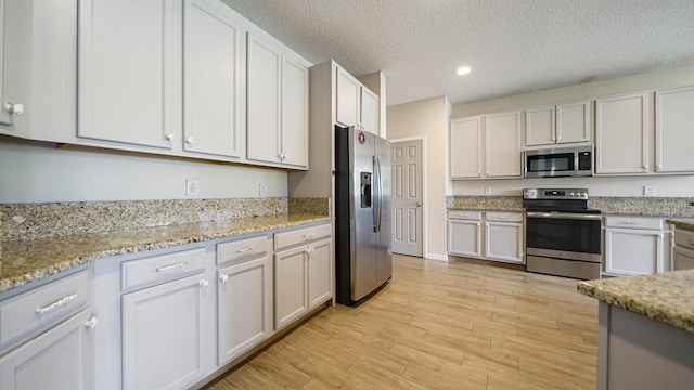 kitchen featuring appliances with stainless steel finishes, white cabinets, light hardwood / wood-style floors, light stone countertops, and a textured ceiling