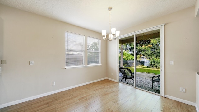 unfurnished room featuring a notable chandelier, a textured ceiling, a healthy amount of sunlight, and light wood-type flooring