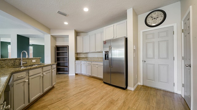 kitchen featuring sink, dark stone countertops, white cabinets, stainless steel fridge, and light hardwood / wood-style flooring