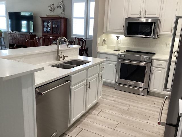 kitchen with white cabinetry, sink, stainless steel appliances, backsplash, and a kitchen island with sink