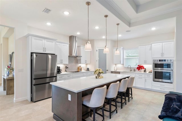 kitchen with visible vents, a kitchen island, wall chimney range hood, white cabinets, and stainless steel appliances