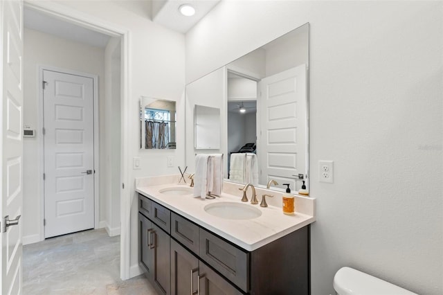 full bathroom with double vanity, toilet, baseboards, and a sink