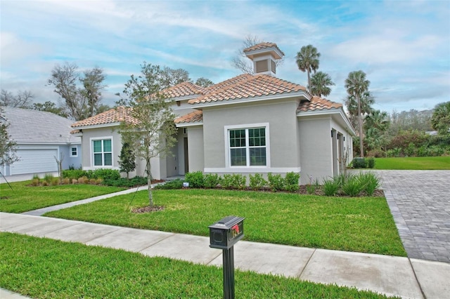 mediterranean / spanish house featuring stucco siding, a tiled roof, decorative driveway, and a front yard