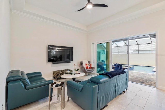 living room with a raised ceiling, a ceiling fan, crown molding, light tile patterned floors, and baseboards