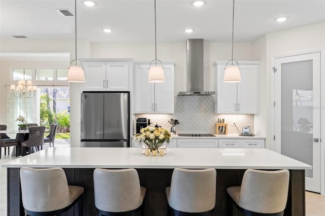 kitchen with visible vents, a kitchen breakfast bar, white cabinetry, freestanding refrigerator, and wall chimney range hood