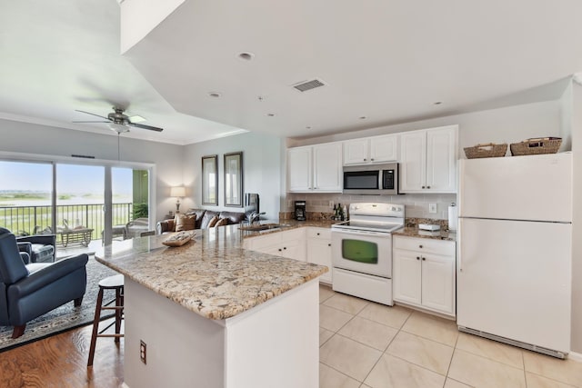 kitchen featuring light stone countertops, sink, kitchen peninsula, white appliances, and decorative backsplash