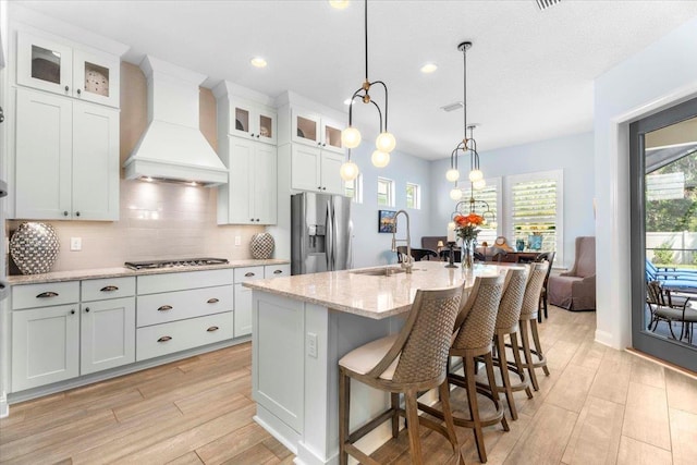 97 Paranza Trce, Saint Augustine, FL 32095 - kitchen with appliances with stainless steel finishes, custom range hood, light wood finished floors, backsplash, and a kitchen island with sink