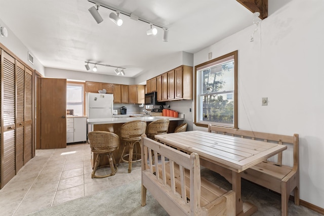 kitchen featuring brown cabinets, light countertops, freestanding refrigerator, black microwave, and a peninsula