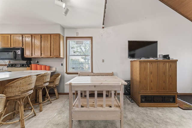 kitchen featuring black microwave, range with electric stovetop, vaulted ceiling, and brown cabinets