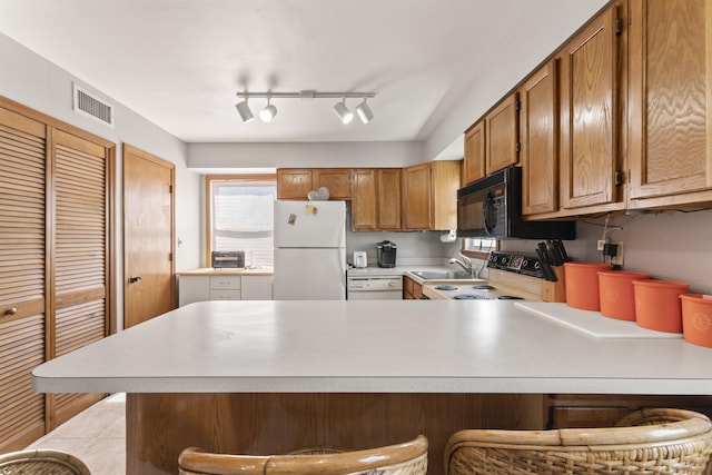 kitchen featuring black microwave, a peninsula, light countertops, and freestanding refrigerator