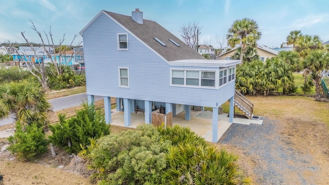 rear view of property with a shingled roof, driveway, stairway, and a carport