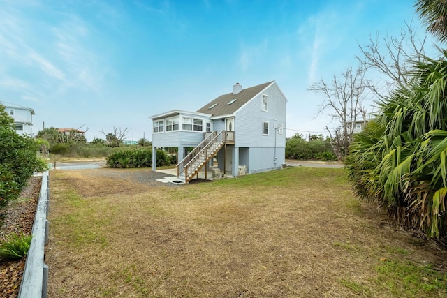 rear view of property with a sunroom, a lawn, a chimney, and stairs