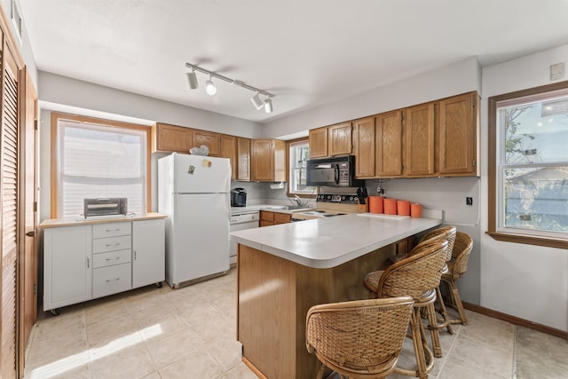 kitchen featuring brown cabinetry, white appliances, light countertops, and a peninsula