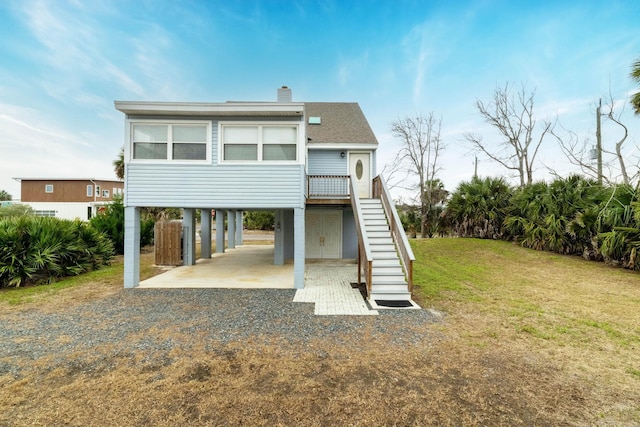 rear view of property featuring driveway, stairway, roof with shingles, a carport, and a chimney