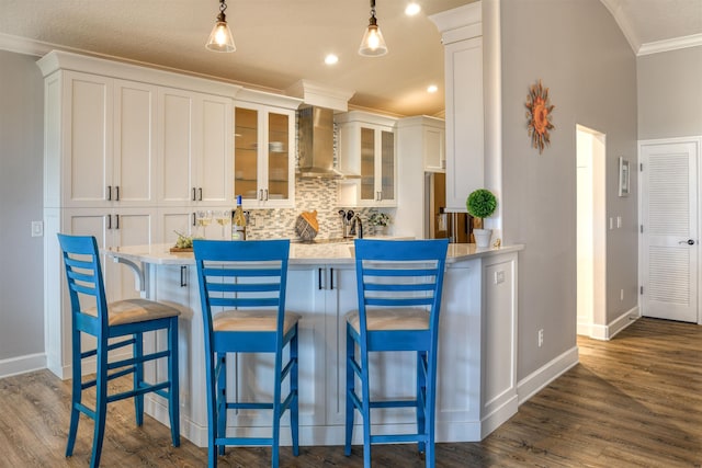 kitchen with wall chimney range hood, hanging light fixtures, white cabinetry, and a breakfast bar area