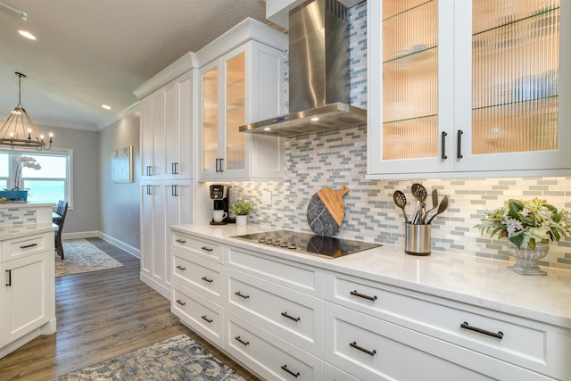 kitchen with hanging light fixtures, black electric stovetop, wall chimney range hood, crown molding, and white cabinetry