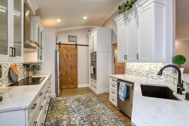 kitchen featuring a barn door, sink, appliances with stainless steel finishes, white cabinets, and wall chimney exhaust hood