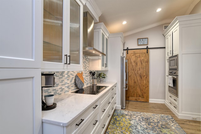 kitchen with appliances with stainless steel finishes, white cabinetry, wall chimney exhaust hood, a barn door, and light stone countertops