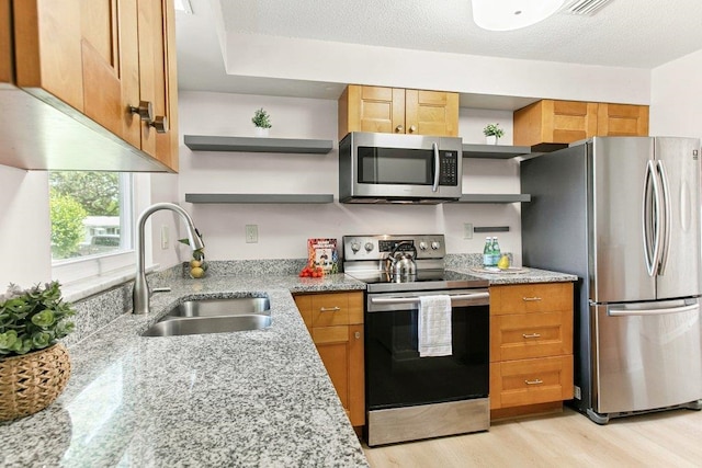 171 Deltona Blvd, Saint Augustine, FL 32086 - kitchen featuring appliances with stainless steel finishes, open shelves, light wood-style flooring, light stone counters, and brown cabinetry