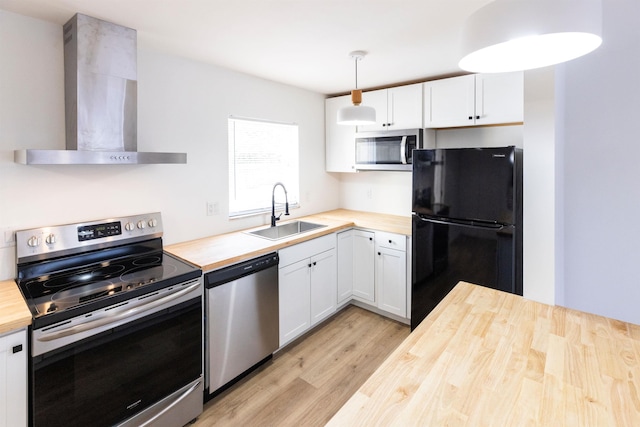 kitchen with sink, white cabinetry, hanging light fixtures, stainless steel appliances, and wall chimney range hood