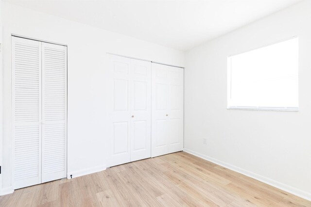 unfurnished bedroom featuring multiple closets and light wood-type flooring