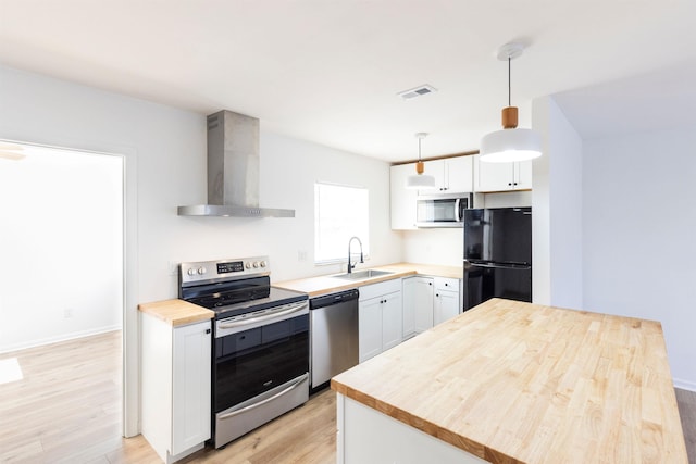 kitchen featuring sink, wall chimney range hood, pendant lighting, stainless steel appliances, and white cabinets