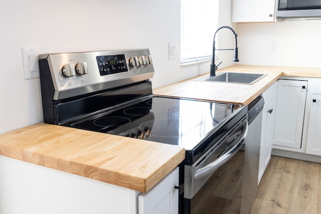 kitchen with sink, stainless steel appliances, light hardwood / wood-style floors, white cabinets, and wood counters