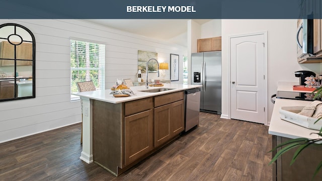 kitchen with dark wood-type flooring, sink, appliances with stainless steel finishes, and an island with sink