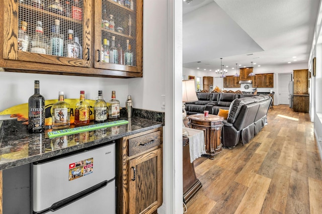 bar featuring stainless steel refrigerator, light hardwood / wood-style flooring, dark stone counters, pendant lighting, and custom exhaust hood