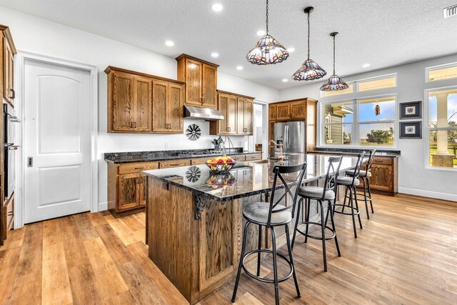 kitchen with light hardwood / wood-style flooring, a kitchen island with sink, hanging light fixtures, and stainless steel appliances