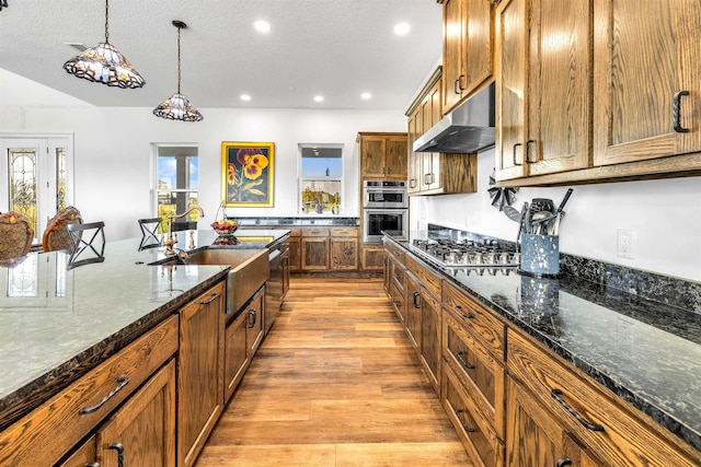 kitchen featuring sink, stainless steel appliances, light hardwood / wood-style flooring, dark stone countertops, and decorative light fixtures