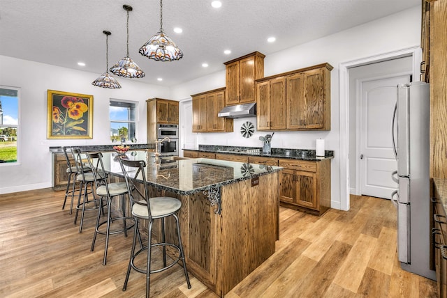 kitchen with a breakfast bar, a kitchen island with sink, hanging light fixtures, light hardwood / wood-style flooring, and a textured ceiling