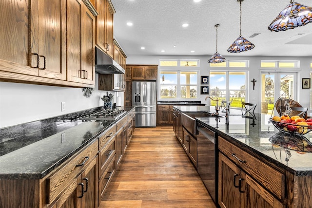 kitchen with a kitchen island with sink, sink, light hardwood / wood-style flooring, dark stone countertops, and stainless steel appliances