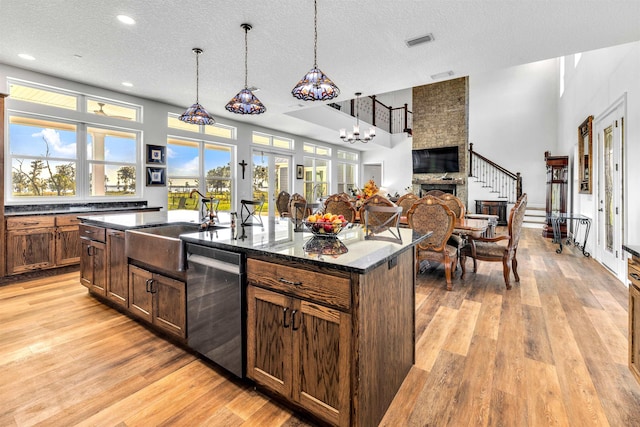 kitchen featuring dishwasher, a textured ceiling, a stone fireplace, and a kitchen island with sink