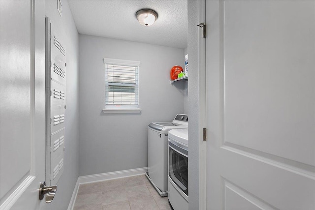 washroom with a textured ceiling, washing machine and dryer, light tile patterned flooring, baseboards, and laundry area