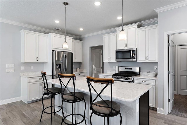 kitchen with visible vents, stainless steel appliances, an island with sink, and ornamental molding