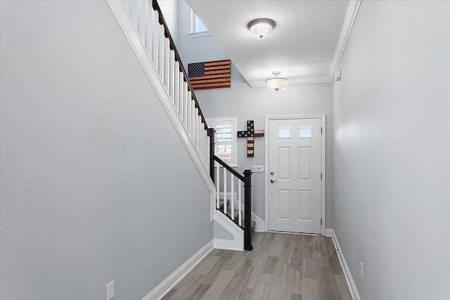 entryway with stairway, wood finished floors, baseboards, a textured ceiling, and crown molding