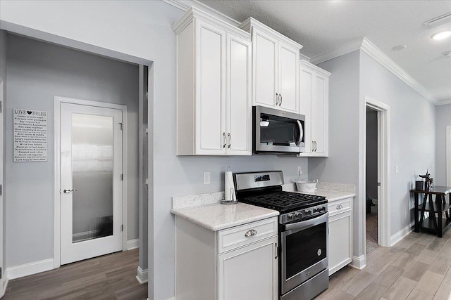 kitchen with baseboards, ornamental molding, white cabinets, appliances with stainless steel finishes, and light wood-type flooring