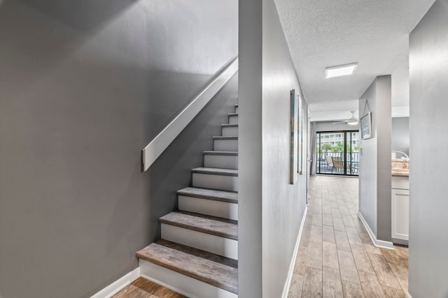 staircase with ceiling fan, wood-type flooring, and a textured ceiling