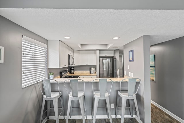 kitchen with a textured ceiling, white cabinets, appliances with stainless steel finishes, dark hardwood / wood-style flooring, and kitchen peninsula