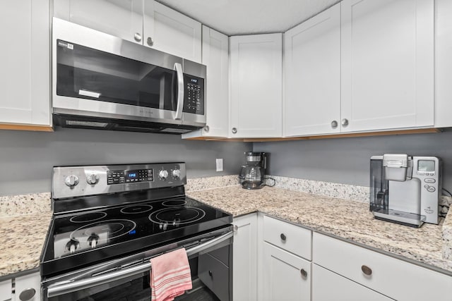 kitchen featuring light stone countertops, white cabinetry, and electric stove