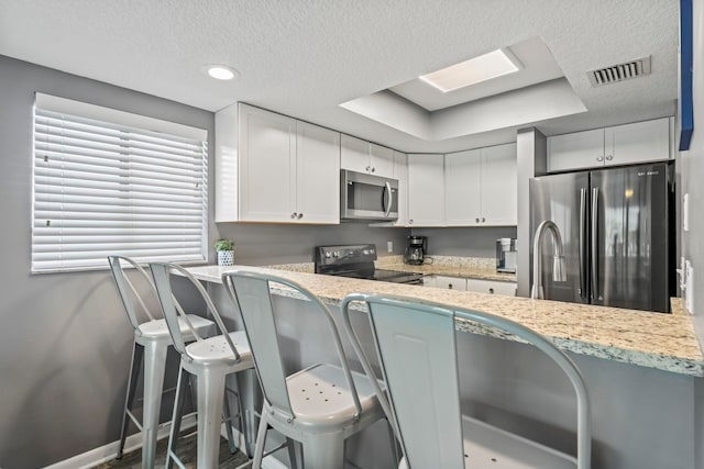 kitchen featuring a breakfast bar, kitchen peninsula, light stone countertops, stainless steel appliances, and white cabinets