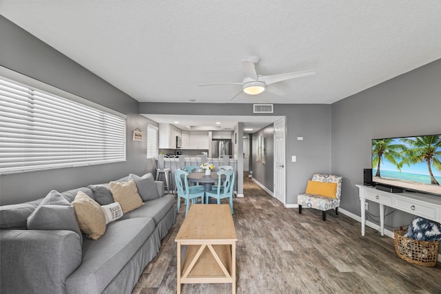 living room featuring ceiling fan, dark wood-type flooring, and a textured ceiling